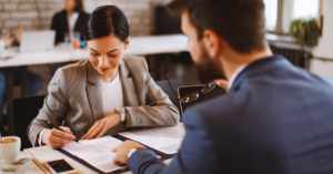 female worker signing contract while male worker points at contract