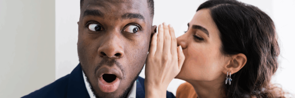 a women at work whispering into her male colleagues ear